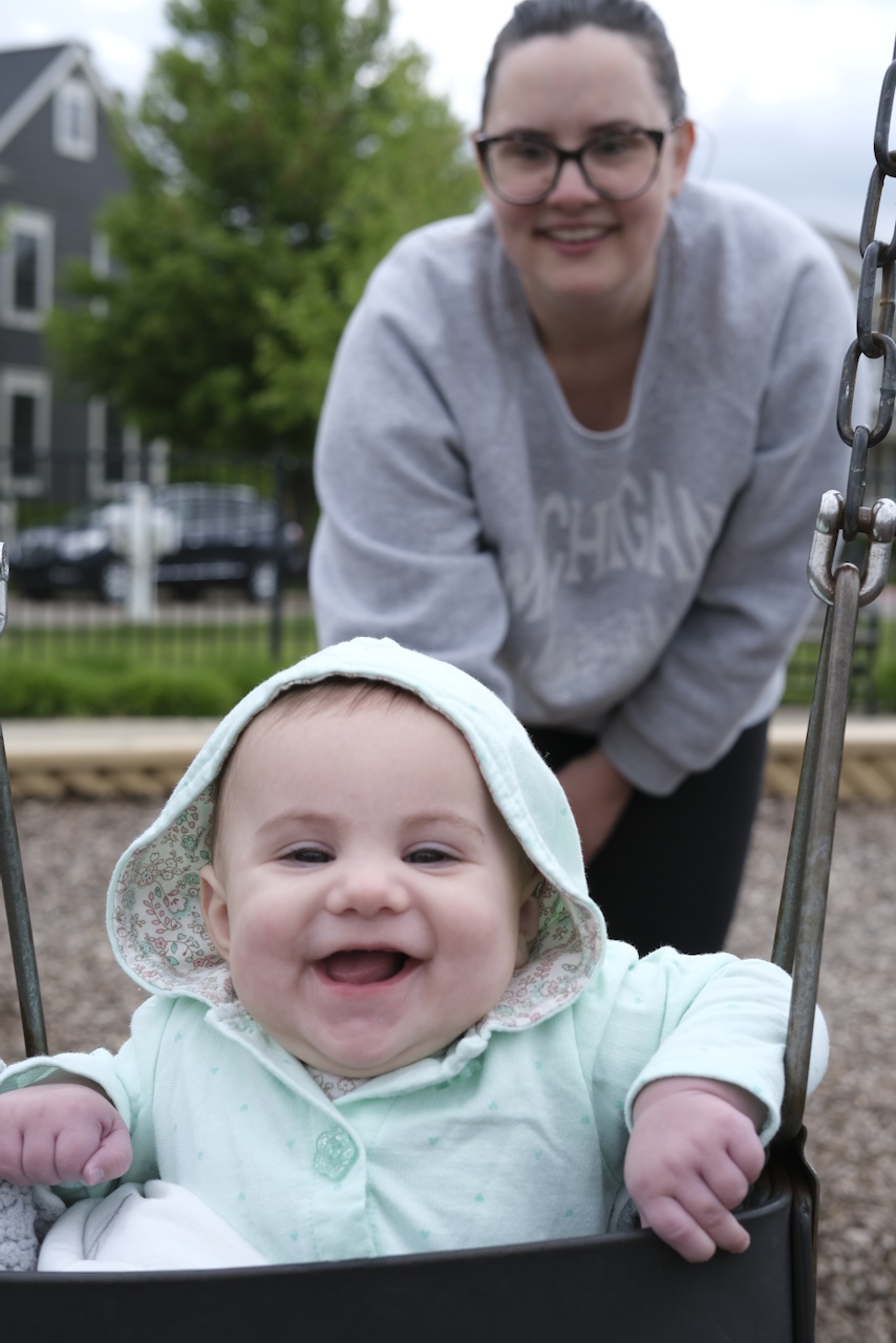 Mom pushing Zoe on a swing. Zoe has a huge grin.